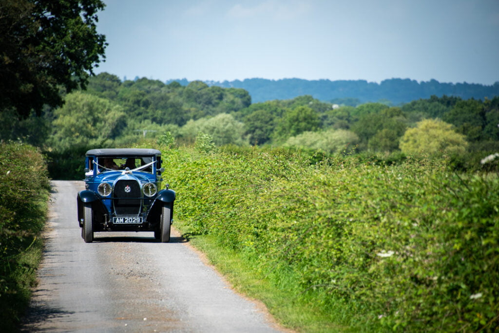 Classic car arriving to wedding ceremony by Nick Ford Photography