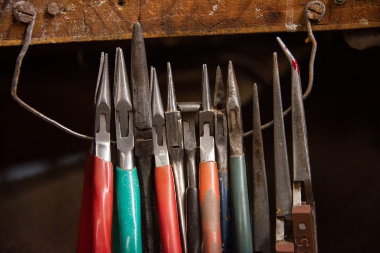 small jewellery pliers , all lined up next to each other of various sizes,length and shape of the nose of the plier, each has a different handle from the colour to the shape.