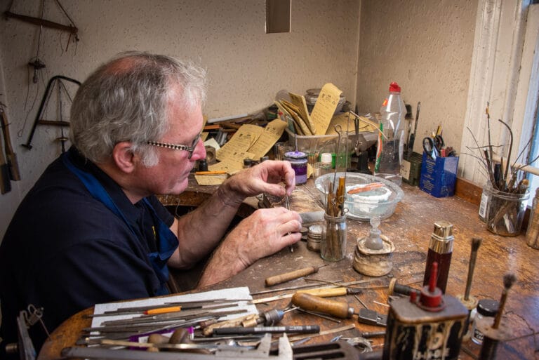 Jewellery repair professional in his workshop, tools are scattered on his workbench where he is carefully fixing a delicate chain.