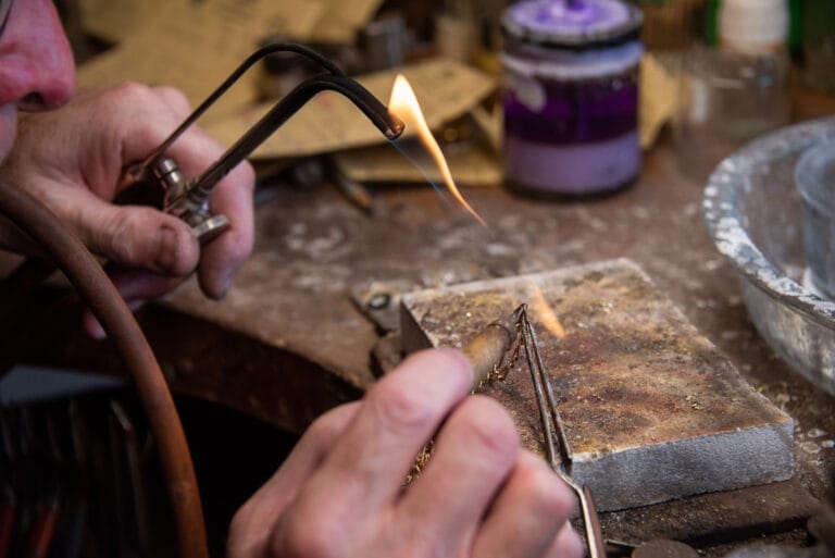 Jewellery repair professional using a blowtorch to carefully repair a chain, capturing the precision and skill involved in the delicate process.