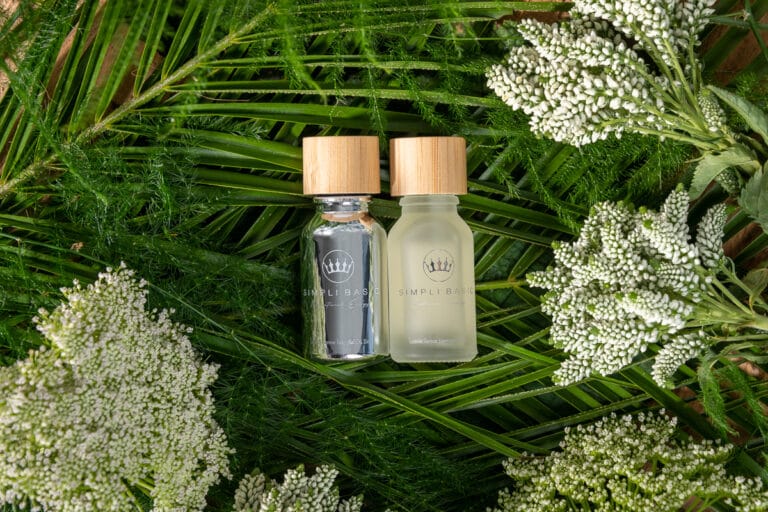 Two bottles of essential oils nestled in a rich bed of lush green foliage, creating a peaceful and earthy vibe that complements the natural qualities of the oils.