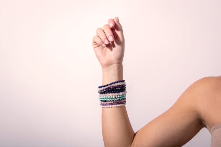 Arm adorned with multiple colorful bracelets, displayed on a simple white background, showcasing the vibrant mix of designs and bold, eclectic style.
