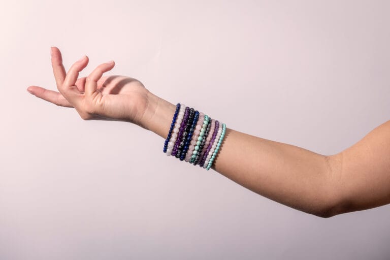 Arm adorned with multiple colorful bracelets, displayed on a simple white background, showcasing the vibrant mix of designs and bold, eclectic style.