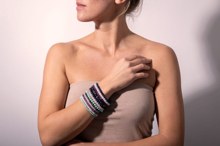 Hand model wearing a tan top, showcasing multiple colourful bracelets stacked together, highlighting the vibrant mix of designs and bold, eclectic style.