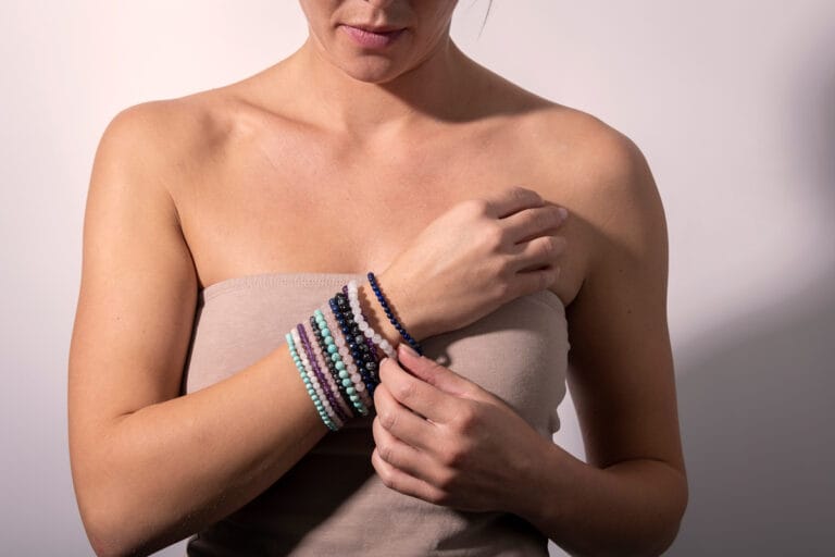 Hand model wearing a tan top, showcasing multiple colourful bracelets stacked together, highlighting the vibrant mix of designs and bold, eclectic style.