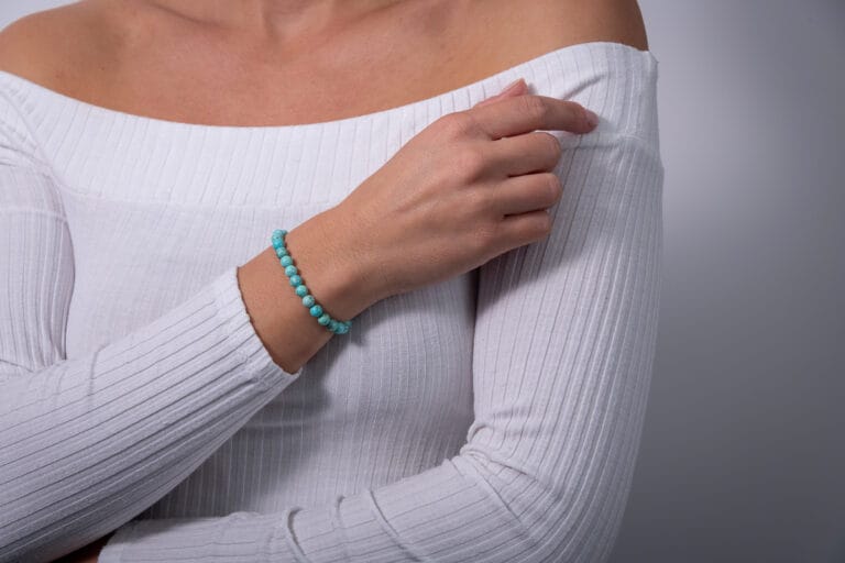 Hand model wearing a white jumper, showcasing a tourquoise beaded bracelet, highlighting the delicate design and elegant style of the jewelry.