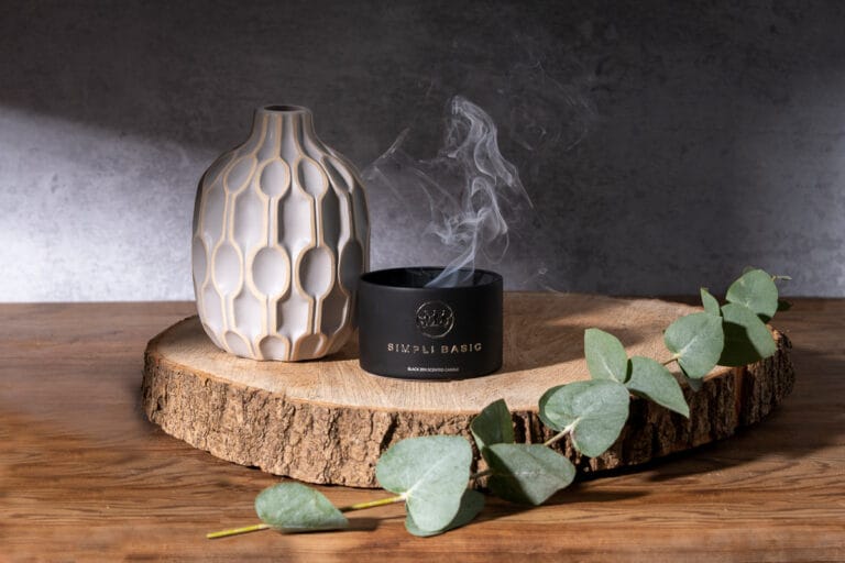 Candle on a round of wood with a vase and foliage, just blown out, with delicate smoke rising, creating a tranquil and atmospheric scene.